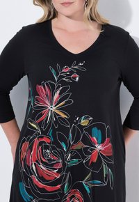 Tunique noire à col en V avec manches trois-quarts, présentant un motif floral multicolore en rouge, rose et turquoise sur le devant. Tissu doux.