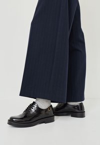 Schwarze Lackleder Schnürschuhe mit runder Spitze und niedrigem Blockabsatz, kombiniert mit grauen Socken und einer navyblauen Nadelstreifenhose.