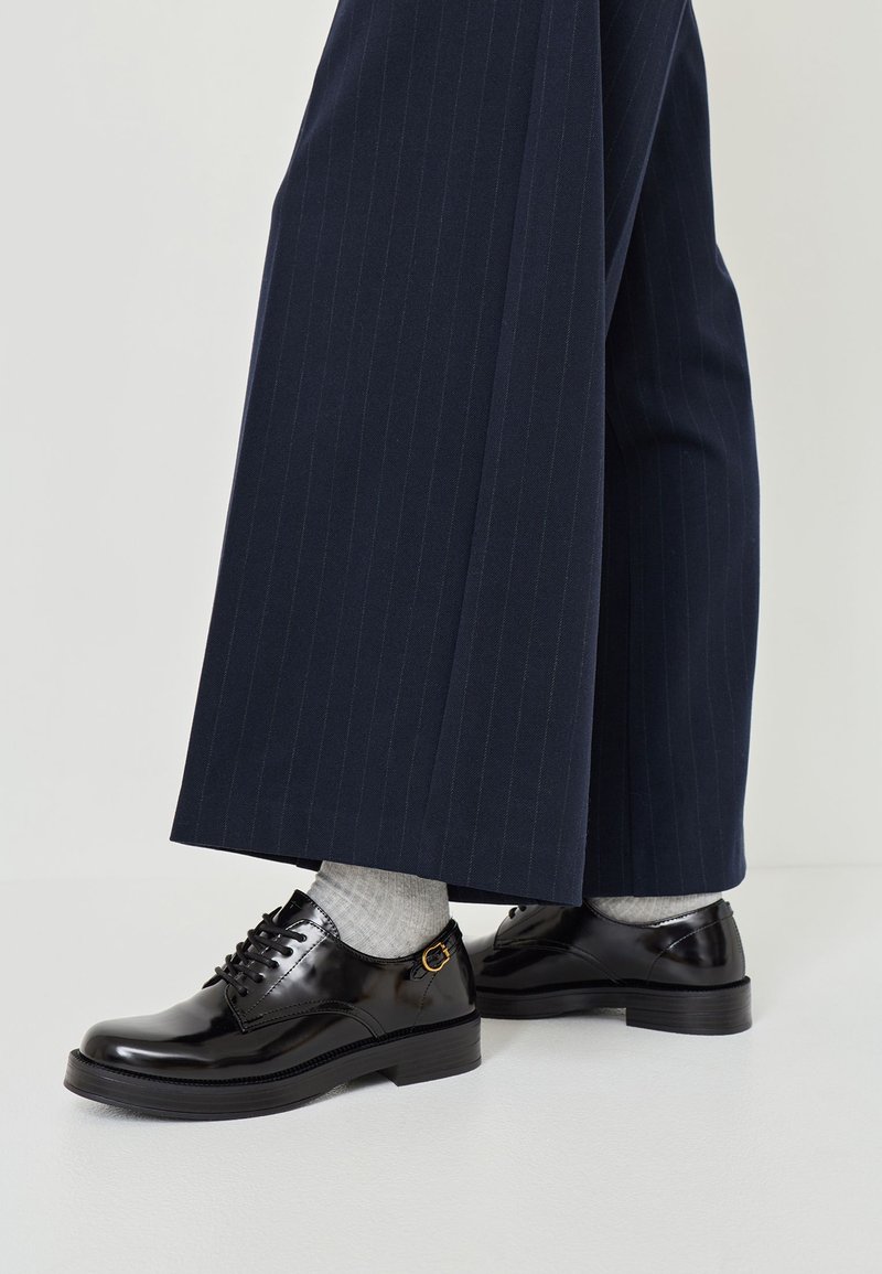Schwarze Lackleder Schnürschuhe mit runder Spitze und niedrigem Blockabsatz, kombiniert mit grauen Socken und einer navyblauen Nadelstreifenhose.