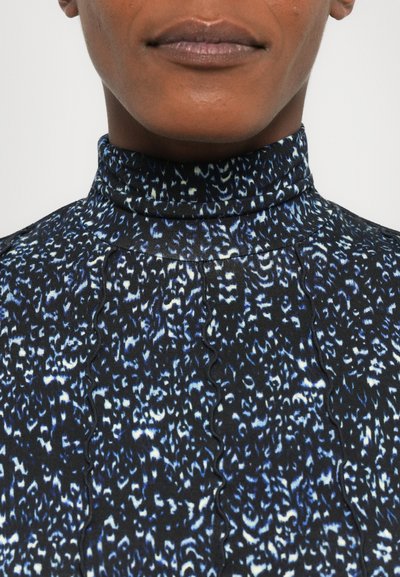 Black high-neck top with a textured fabric featuring a blue and white abstract pattern, scalloped detailing along the seams.
