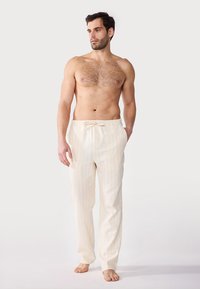 Lys beige loungebukser med tynne vertikale striper, med elastisk snor i livet og sidelommer, laget av mykt stoff.