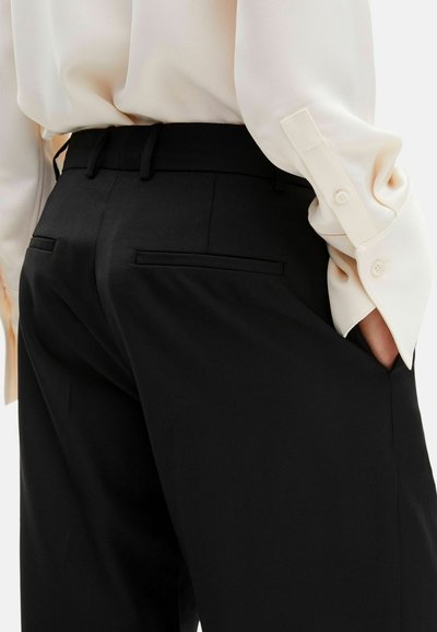 Czarne, dopasowane spodnie garniturowe o gładkiej fakturze, z bocznymi kieszeniami i dopasowaną talią, zestawione z jasnokolorową bluzką z długim rękawem.