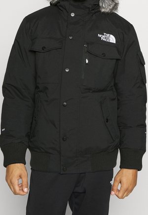 Czarna zimowa kurtka z kapturem obszytym futrem, zapinana na guziki z przodu, z wieloma kieszeniami oraz logo "The North Face" na piersi.