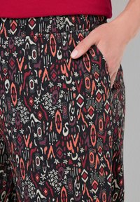 Černá tkanina s geometrickým vzorem v červené, oranžové a bílé barvě. Elastický pas s bočními kapsami, hladká textura.