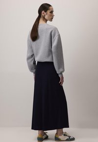 Felpa grigia chiaro con spalle basse, abbinata a una lunga gonna blu scuro. Calzature comode e casual con accenti verdi e gialli.