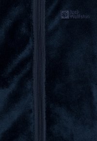 Veste en polaire navy avec une fermeture éclair sur toute la longueur, présentant une texture lisse et un logo brodé sur le côté gauche supérieur.