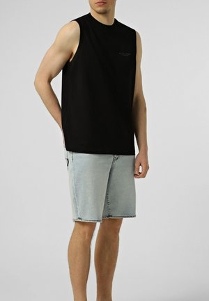 Un mannequin homme se tient devant un fond uni, vêtu d’un haut noir sans manches et d’un short en jean bleu clair.