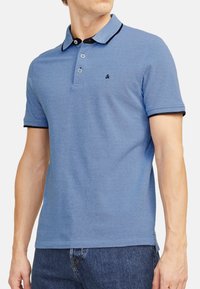 Blauwe polo shirt van gestructureerde stof, met korte mouwen, een met zwart afgewerkte kraag en een sluiting met drie knopen. Klein logo op de borst.