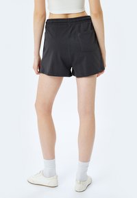 Zwarte shorts met een elastische tailleband, voorzien van een achterzak en een relaxed fit, gemaakt van lichtgewicht stof. G gedragen met witte schoenen en sokken.
