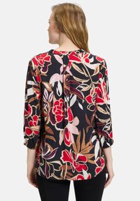 Zwarte bloes met driekwartmouwen. Heeft oversized bloemen in rood, roze en beige en een relaxte pasvorm met een afgeronde zoom.