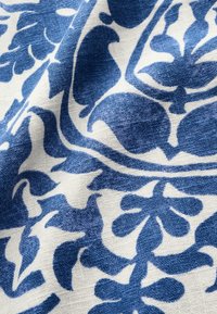 Puuvillakangas, jossa on sinivalkoinen kukkakuviointi, monimutkaisia käyriä ja muotoja, teksturoituna pellavapohjaan.