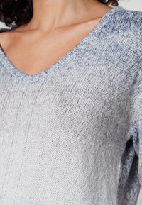 Pull en tricot bleu clair avec un col en V et des bords côtelés ; présente un motif texturé et une coupe ample, mettant en avant la douceur et le confort.