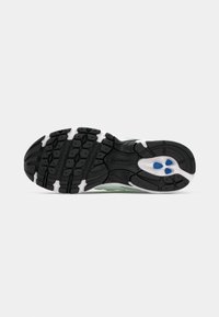 Semelle d’une chaussure de course New Balance avec une bande de roulement noire, des accents blancs et trois formes ovales bleues près du talon sur un fond uni.