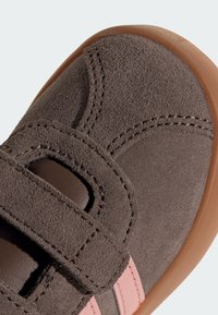 Gros plan sur une chaussure pour tout-petit en daim marron avec une bride Velcro et des accents roses sur le bord de la semelle en caoutchouc.