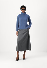 Blauer, gerippter Rollkragenpullover mit langen Ärmeln, kombiniert mit einem grauen, bodenlangen Rock. Schwarze High Heels runden das Outfit ab.