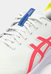 White athletic shoe with a textured upper, featuring a pink ASICS logo, blue laces, and a subtle design. Sole is predominantly white.