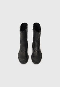 Par de botas de couro pretas até o meio da panturrilha com detalhes em nervuras na frente e zíperes laterais, vistas de cima sobre um fundo claro.