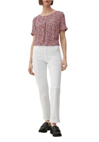 Kurze blauen Bluse mit rotem Blumenmuster, kombiniert mit weißen geraden Jeans und schwarzen Mokassins. Der Stoff scheint leicht und strukturiert zu sein.