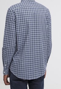 Blå och grön rutig skjorta med långa ärmar, knäppning vid ärmslut och en rundad nederkant. Tyget har en glatt textur med ett klassiskt rutmönster.