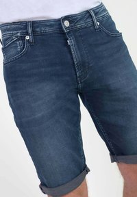 Shorts de denim en azul oscuro, con dobladillos enrollados, bolsillos frontales y cierre de botón, de textura suave y ligera decoloración.