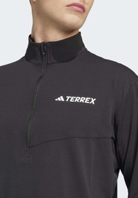 Black half-zip pullover featuring a high collar, lightweight fabric, and a white "TERREX" logo on the chest with a smooth texture.