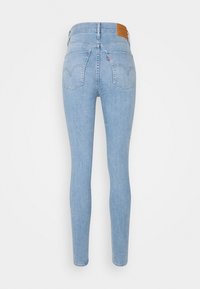 Jean skinny bleu clair taille haute avec poches arrière, passants de ceinture et patch en cuir marron sur la ceinture.