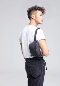 Borsa a tracolla grigia realizzata in tessuto testurizzato con una forma curva, indossata diagonalmente sul corpo. Presenta un accento colorato e un logo.