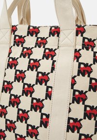Sac fourre-tout en toile avec une base beige, présentant un motif de cœurs rouges et "DKNY" en noir, coutures renforcées et poignées solides.