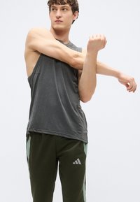 Top atlético cinza sem mangas com um corte descontraído e racha lateral, combinado com calças de jogging verde-escuro com detalhes laterais verdes claros e logótipo.