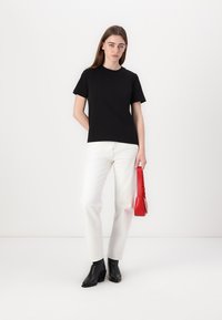 Svart bomull T-skjorte med korte ermer, kombinert med hvite jeans. Holder en liten rød veske. Svarte ankelstøvler fullfører antrekket.