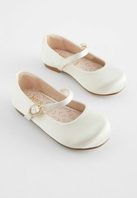 Ballet flats blanches en matériau lisse, avec une sangle décorative ornée d'une boucle ronde agrémentée de pierres. Doublure intérieure rose doux.