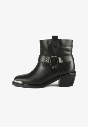 Bottine en cuir noir avec un talon haut, dotée d'une large sangle en cuir avec des finitions en métal argenté et d'un design à bout pointu.