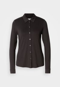 Chemise noire à manches longues avec col pointu et sept boutons visibles sur le devant.