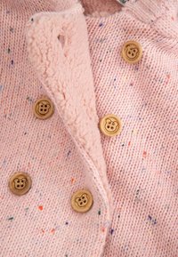 Jasnoróżowy, dziergany kardigan z wielokolorowymi plamkami, z miękkim kołnierzem z polaru i pięcioma drewnianymi guzikami z wzorem niedźwiedzia.