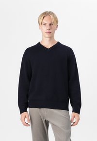 Pull en V marine avec des poignets et un ourlet côtelés, fabriqué en tissu doux, associé à un pantalon en velours côtelé de couleur claire. Design simple et classique.