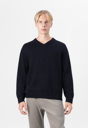 Marineblauer V-Ausschnitt-Pullover mit gerippten Bündchen und Saum, aus weichem Stoff, kombiniert mit hellen Cordhosen. Einfaches und klassisches Design.