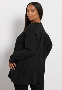 Czarna bluzka z długim rękawem o luźnym kroju, wykonana z miękkiego materiału. Posiada okrągły dół i opadnięte ramiona dla dodatkowego komfortu.