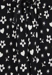 Black fabric with white floral and heart patterns; textured, lightweight material with a drawstring detail at the waist.