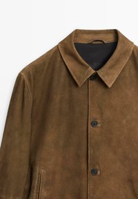 Brun mockajacka med spetsig krage, fem svarta knappar och sidofickor; har en mjuk, texturerad yta och ett svart innerfoder.