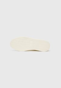 Rubber shoe sole in off-white with a textured herringbone pattern; features a small rectangular logo in the center.