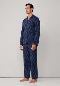 Conjunto de pijama azul marino fabricado en una tela suave, con un patrón de estrellas claras, que incluye una camisa de botones de mangas largas y pantalones de pierna recta.