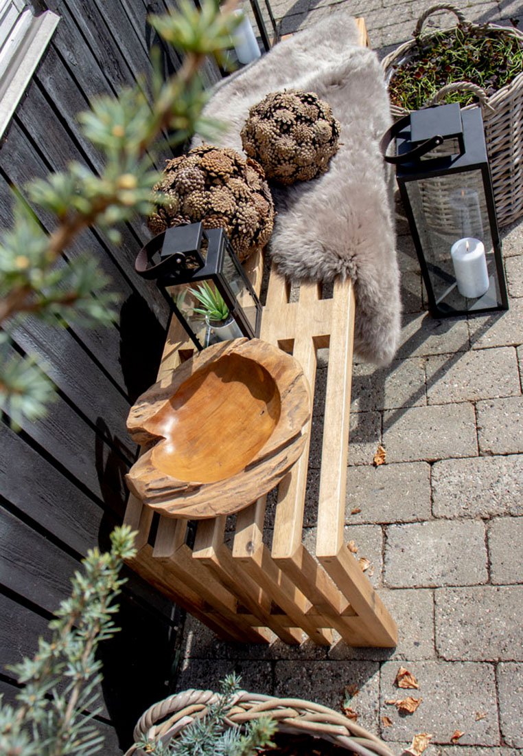 Holzlattenbank mit heller Oberfläche, kombiniert mit einer runden, geschnitzten Holzschale. Dekoriert mit Kunstfell, Laternen und natürlichen Elementen.