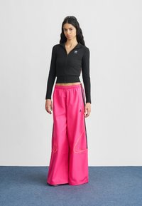 Fekete, cipzáras, hosszú ujjú felső, élénk rózsaszín, széles szárú nadrággal, amelyen fekete oldalsávok és sárga varrásdíszek vannak.