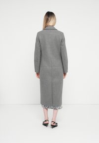 Grijze lange jas met een getailleerde pasvorm en brede revers. Gemaakt van textiel met structuur, heeft een rechte snit en wordt gedragen over een bloemenpatroon.