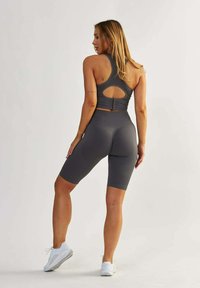 Grijze naadloze sportset bestaande uit een geribbelde tanktop met een open rug en bijpassende hoge fietsbroek. Inclusief witte sneakers.