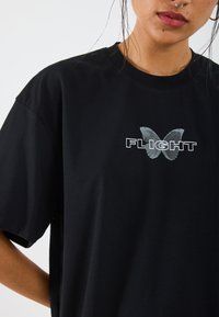 Black cotton t-shirt featuring a graphic design of a butterfly and the word "FLIGHT" in contrasting white lettering. Short sleeves, relaxed fit.