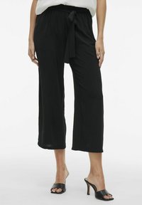 Black, wide-leg pants with a soft texture, featuring a drawstring waistband. Worn with black heeled sandals. Simple and relaxed design.