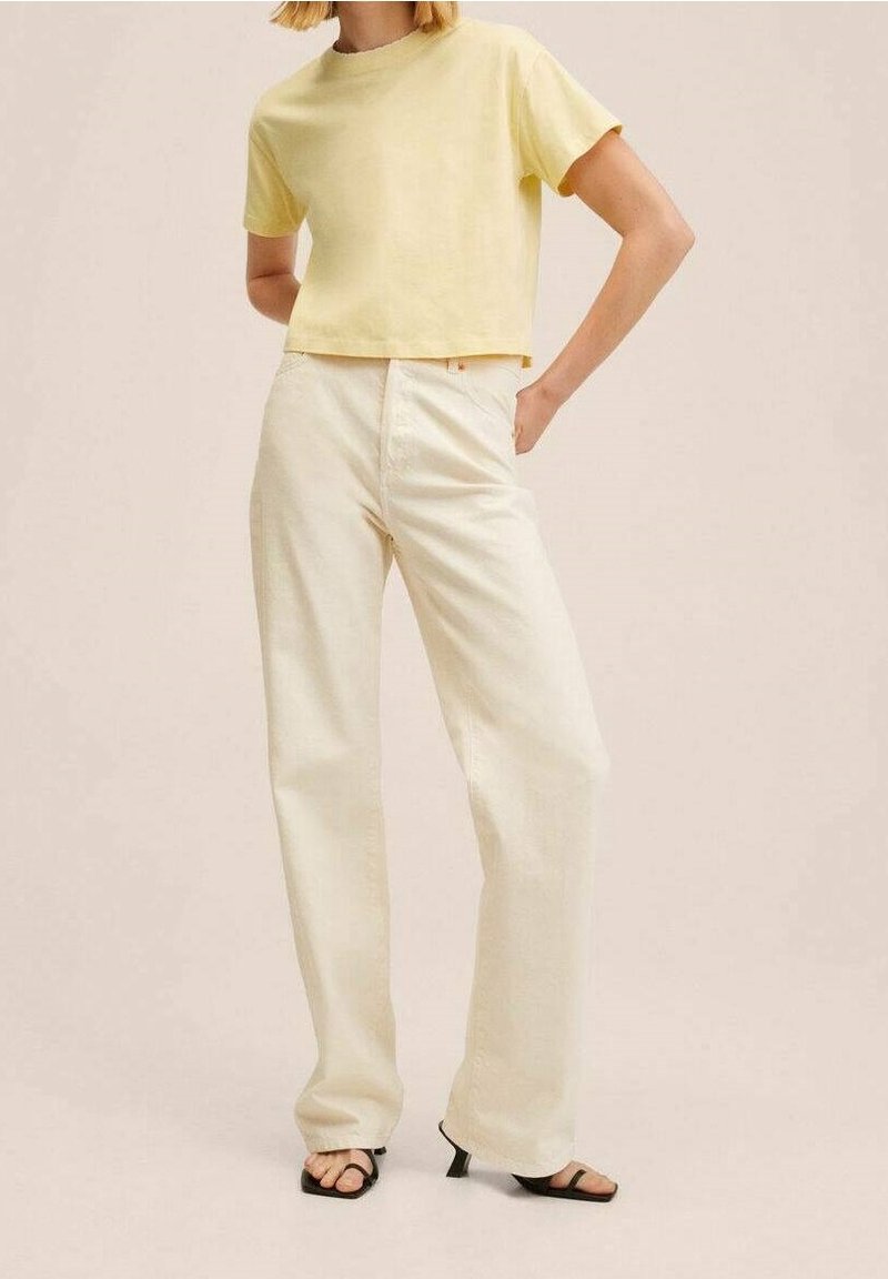 Žluté zkrácené tričko s krátkým rukávem, spárované s krémovými širokými kalhotami. Černé sandály na pásku doplňují tento ležérní outfit.