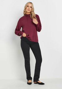 Top a maniche lunghe color malva con collo alto e dettaglio arricciato, abbinato a pantaloni neri attillati e scarpe flat nere. Tessuto liscio, vestibilità comoda.