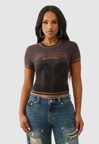 Czarny krótki T-shirt z złotym przeszyciem, z napisem "True Religion Brand Jeans" i dużą cyfrą "02". Noszony z przetartymi niebieskimi dżinsami.